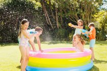 Father and children playing with water guns in backyard — Stock Photo