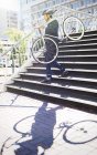 Бізнесмен в костюмі і шоломі, що несе велосипед вниз по міських сходах — стокове фото