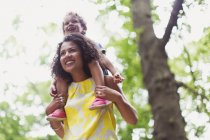 Smiling mother carrying son on shoulders below tree — Stock Photo