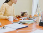 Girl in mouse ears headband watching mother work at computer — Stock Photo