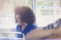 Улыбающаяся женщина с афротекстом и сотовым телефоном в автобусе — стоковое фото