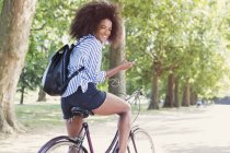 Портрет усміхненої жінки, що їде на велосипеді з mp3 плеєром та навушниками у парку — стокове фото