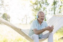 Uomo anziano con cuffie ascoltare musica con lettore mp3 su amaca estiva — Foto stock