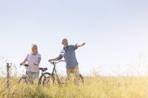 Casal sênior andar de bicicleta no campo rural ensolarado sob o céu azul — Fotografia de Stock