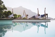Jovens pessoas atraentes praticando ioga na beira da piscina — Fotografia de Stock