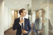Confident businessman adjusting tie in office corridor — Stock Photo