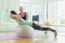 Personal trainer guiding woman doing back extensions on fitness ball — Stock Photo