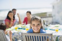 Menina sorridente à mesa no pátio ensolarado — Fotografia de Stock