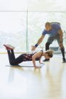 Personal trainer guiding woman doing push-ups on knees at gym — Stock Photo
