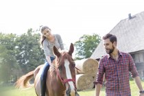 Man leading woman horseback riding in rural pasture — Stock Photo