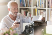 Homme âgé buvant du vin à la machine à écrire dans l'étude — Photo de stock