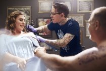 Tattoo artist tattooing woman shoulder at studio — Stock Photo