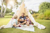 Pai feliz e crianças relaxando no teepee no quintal — Fotografia de Stock
