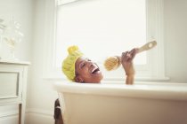 Verspielte reife Frau singt in Luffa-Bürste in Badewanne — Stockfoto
