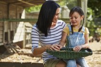 Mother and daughter with basket of eggs outside chicken coop — Stock Photo