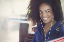 Улыбающаяся женщина с афро слушает музыку в наушниках в автобусе — стоковое фото