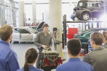 Meccanico spiegando motore auto agli studenti in officina di riparazione auto — Foto stock
