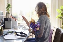 Woman receiving flower bouquet and reading card in home office — Stock Photo