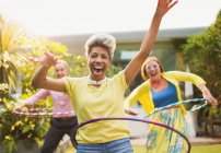 Portrait playful mature adults spinning with plastic hoops in garden — Stock Photo