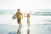 Padre e hija llevando tabla de surf y bodyboard en la playa - foto de stock