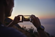 Homme photographiant coucher de soleil vue sur l'océan avec téléphone appareil photo — Photo de stock