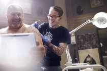 Uomo sorridente con tablet digitale che si fa tatuare la spalla in studio — Foto stock