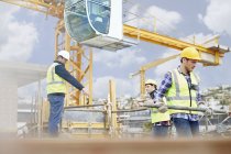 Foreman guiding construction workers below crane at construction site — Stock Photo