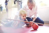Physical therapist guiding boy rolling ball with stick — Stock Photo