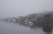 Fog surrounding houses and boats on river — Stock Photo