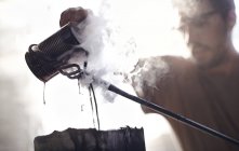 Blacksmith pouring steaming liquid over wrought iron — Stock Photo