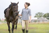 Улыбающаяся женщина, ходящая лошадь на сельском пастбище — стоковое фото