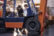 Mecánica examinando carretilla elevadora en taller de reparación de automóviles - foto de stock