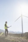 Empresario examinando turbina eólica en paisaje rural - foto de stock
