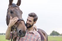 Uomo sorridente che abbraccia cavallo — Foto stock