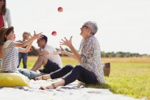 Grand-mère et petit-fils jonglant avec des pommes sur une couverture de pique-nique dans un champ ensoleillé — Photo de stock