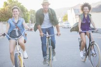 Smiling friends riding bicycles on street — Stock Photo