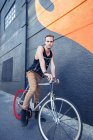 Portrait serious young man on bicycle next to urban graffiti wall — Stock Photo