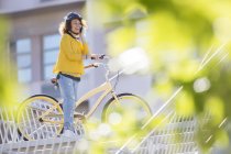 Улыбающаяся женщина разговаривает по мобильному телефону на велосипеде в городе — стоковое фото