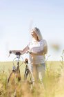 Старша жінка з велосипедом дивиться в сонячне поле — стокове фото