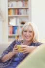 Портрет улыбающейся пожилой женщины, пьющей кофе на диване — стоковое фото