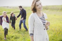 Portrait femme souriante tenant des fleurs sauvages dans la prairie avec la famille — Photo de stock