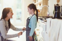 Mother tying apron on daughter in kitchen — Stock Photo