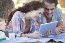 Couple using digital tablet on blanket outdoors — Stock Photo