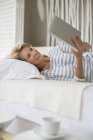 Donna anziana che utilizza tablet digitale sul letto — Foto stock