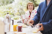 Усміхнена зріла жінка п'є каву в халаті на сніданок — стокове фото