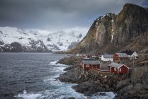 Montagnes enneigées derrière un village de pêcheurs escarpé sur la baie, Hamnoya, Îles Lofoten, Norvège — Photo de stock