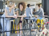 Amigos sonrientes pasando el rato tomando café en la barandilla del patio de la cafetería cerca de bicicletas - foto de stock