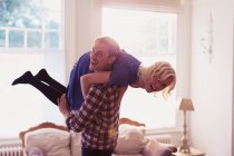 Porträt verspielter Ehemann trägt Frau im Wohnzimmer über die Schulter — Stockfoto