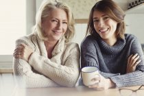 Retrato sonriente madre e hija en suéteres tomando café en la cocina - foto de stock