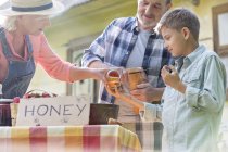 Abuelos y nietos degustando y vendiendo miel en el mercado de granjeros - foto de stock